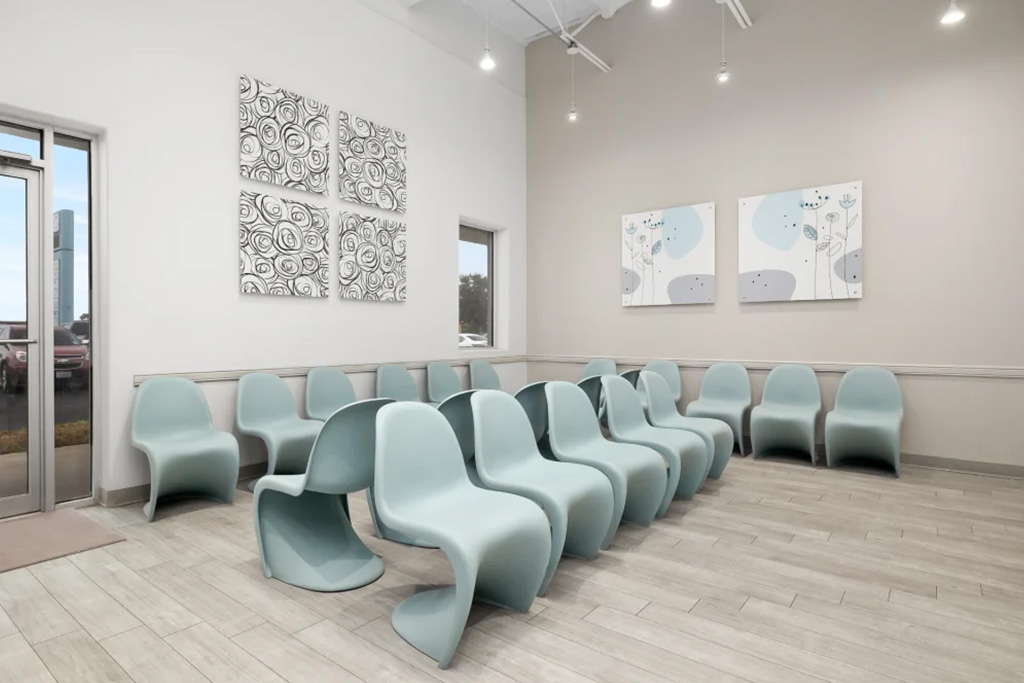 The image depicts an interior space with a row of chairs and a wall featuring artwork.
