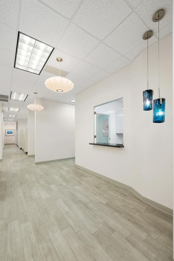 The image shows an interior view of a brightly lit office space with tiled floors, white walls, and modern lighting fixtures.