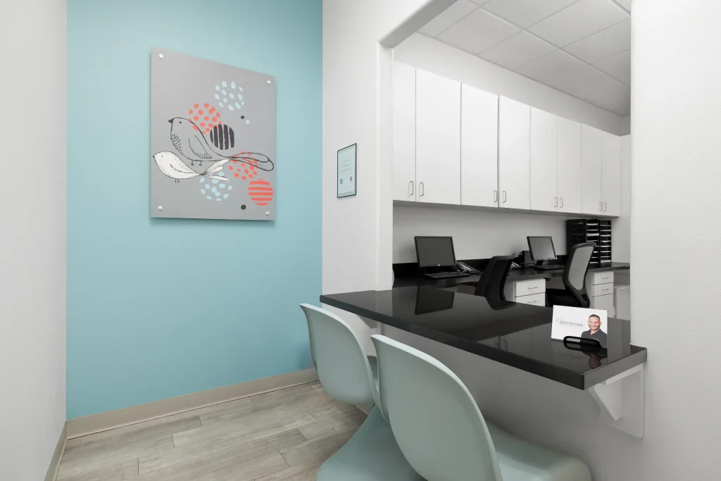 The image shows an interior view of a modern office space with a reception desk and chairs, featuring a blue wall and a framed painting on it.
