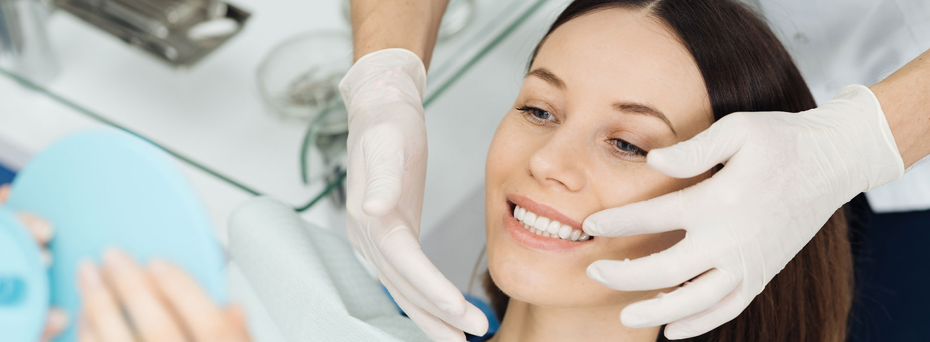 The image shows a woman receiving a facial treatment with the assistance of a professional who is wearing protective gloves.