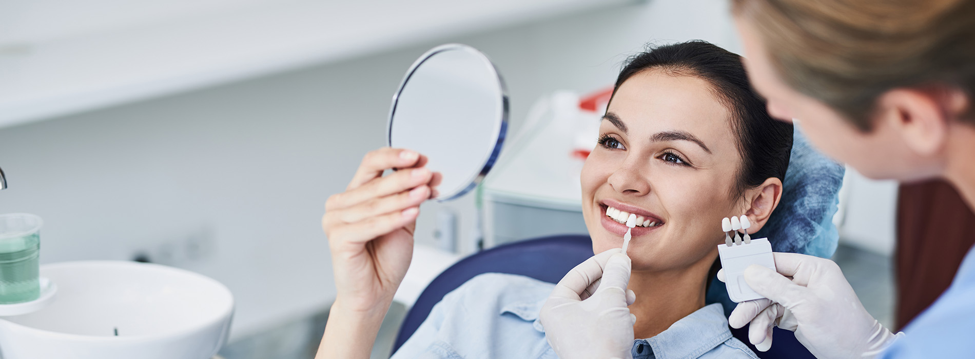 A person is seated in a dental chair, receiving care from a dental professional who stands behind them.