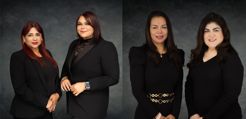 The image shows four women posing together in formal attire, likely for an official event or professional setting. They appear to be smiling and are standing against a backdrop that suggests they are at a conference or similar gathering.