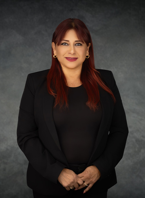 The image shows a woman with red hair, wearing a black blazer, standing against a gray background.