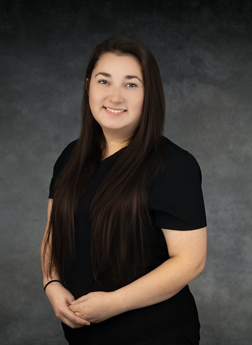 A smiling woman with long hair, wearing a black top and standing against a dark background.