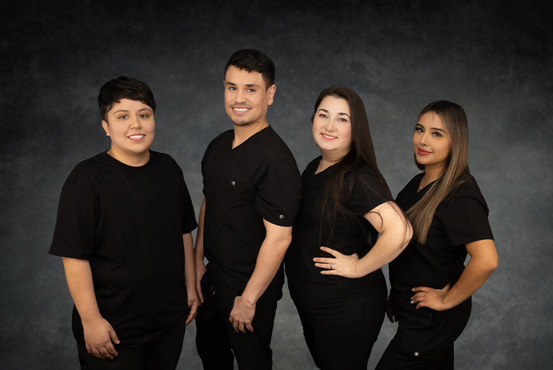 The image shows four individuals posing together, likely professional healthcare workers, with a backdrop suitable for a formal portrait.