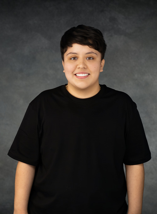 The image shows a person standing in front of a background with a neutral expression on their face.